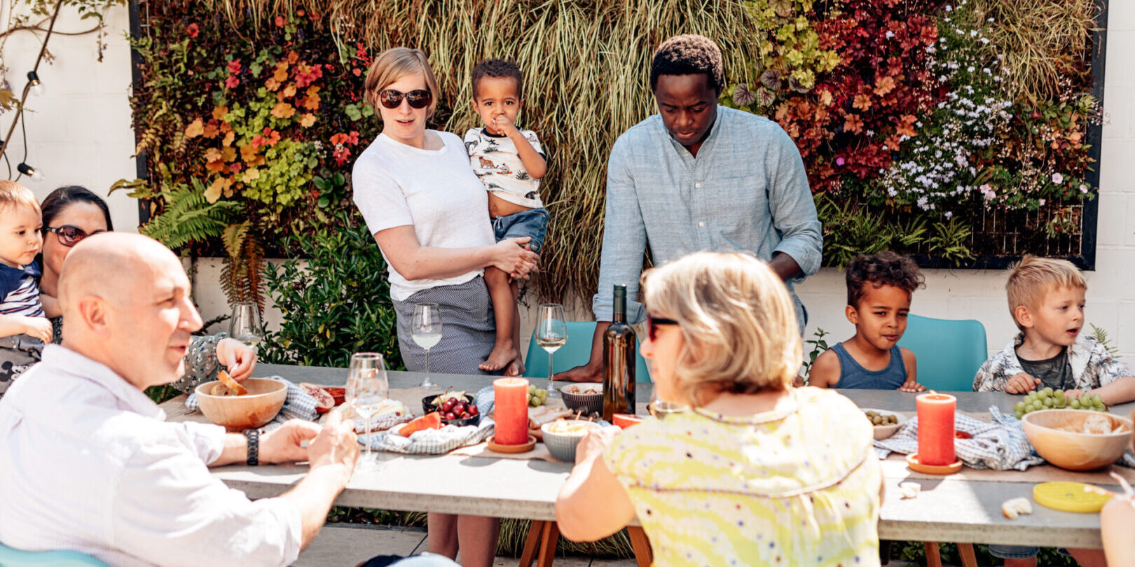 family, friends, adults, and kids having fun sitting or standing around the table on a sunny summer day.